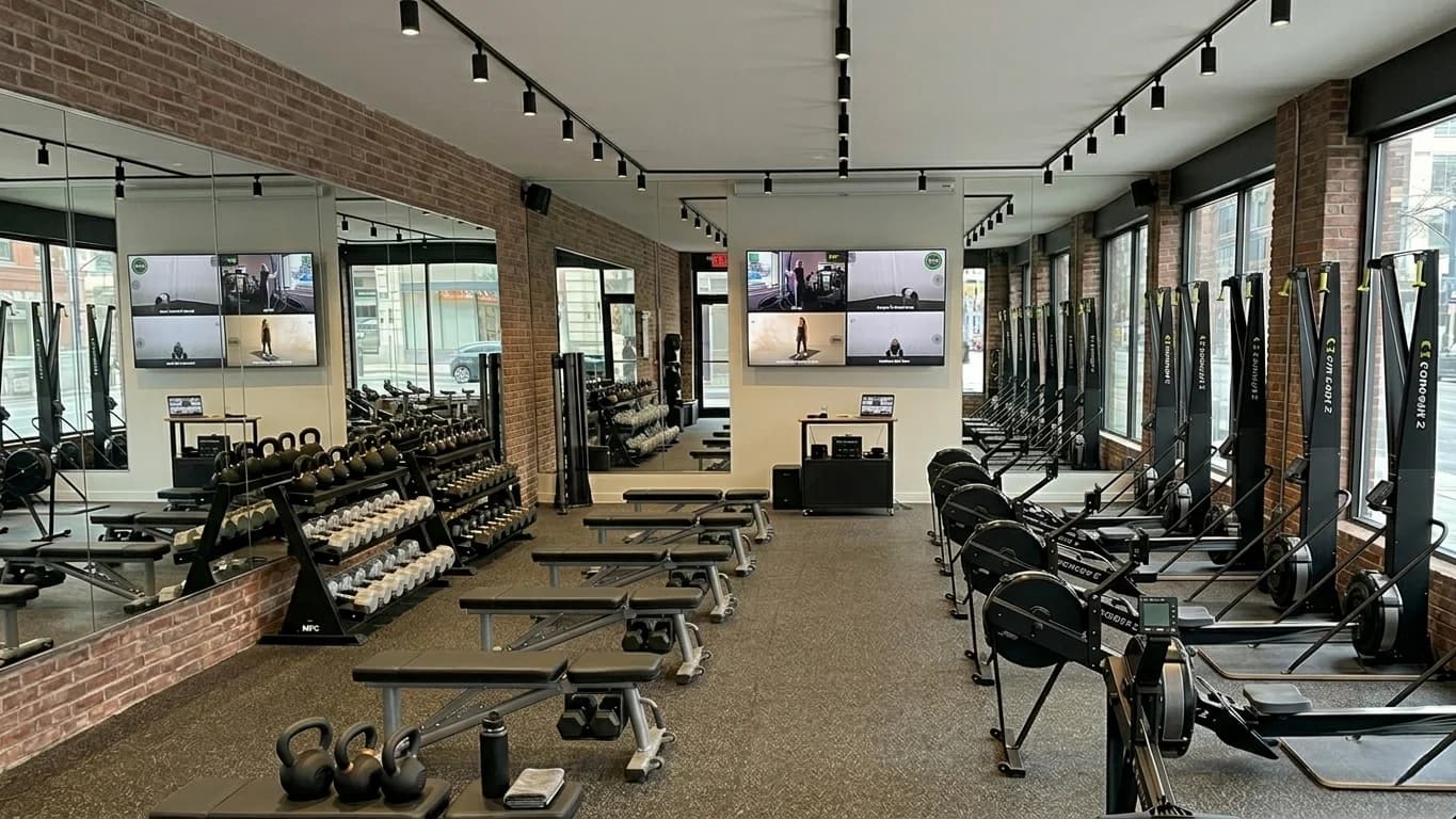 Modern gym floor with multiple TV screens showing workout displays across training zones